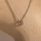 The Cable Circle Charm Necklace in Silver features a circular pendant, ideal for layering or wearing as a statement piece, and is displayed on a beige textured mannequin bust.