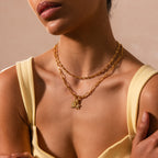 A woman, shown from the shoulders up in a pale yellow top, wears two gold chain necklaces including the Rolo Circle Figaro Necklace.