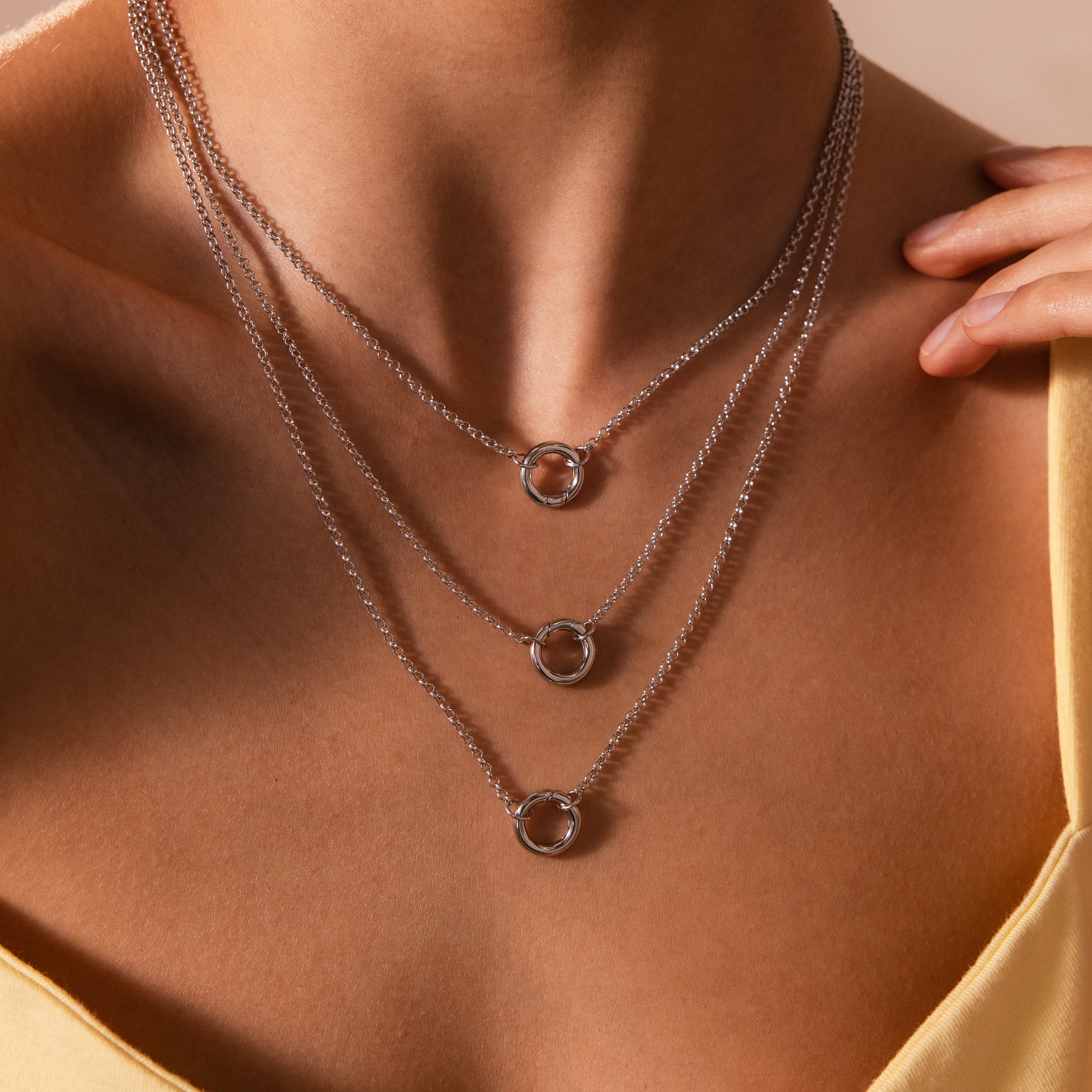 A woman in a yellow top models a layer necklace with three silver chains, circular pendants, including a statement charm and the Cable Circle Charm Necklace in Silver.