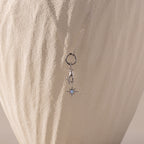 Silver necklace with a charm of a hand holding an opal-centered star, displayed against a textured, cream-colored background