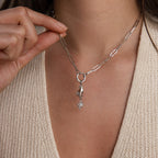 Model wearing a silver paperclip chain necklace with a charm of a hand holding a star pendant, holding the chain near her collarbone.