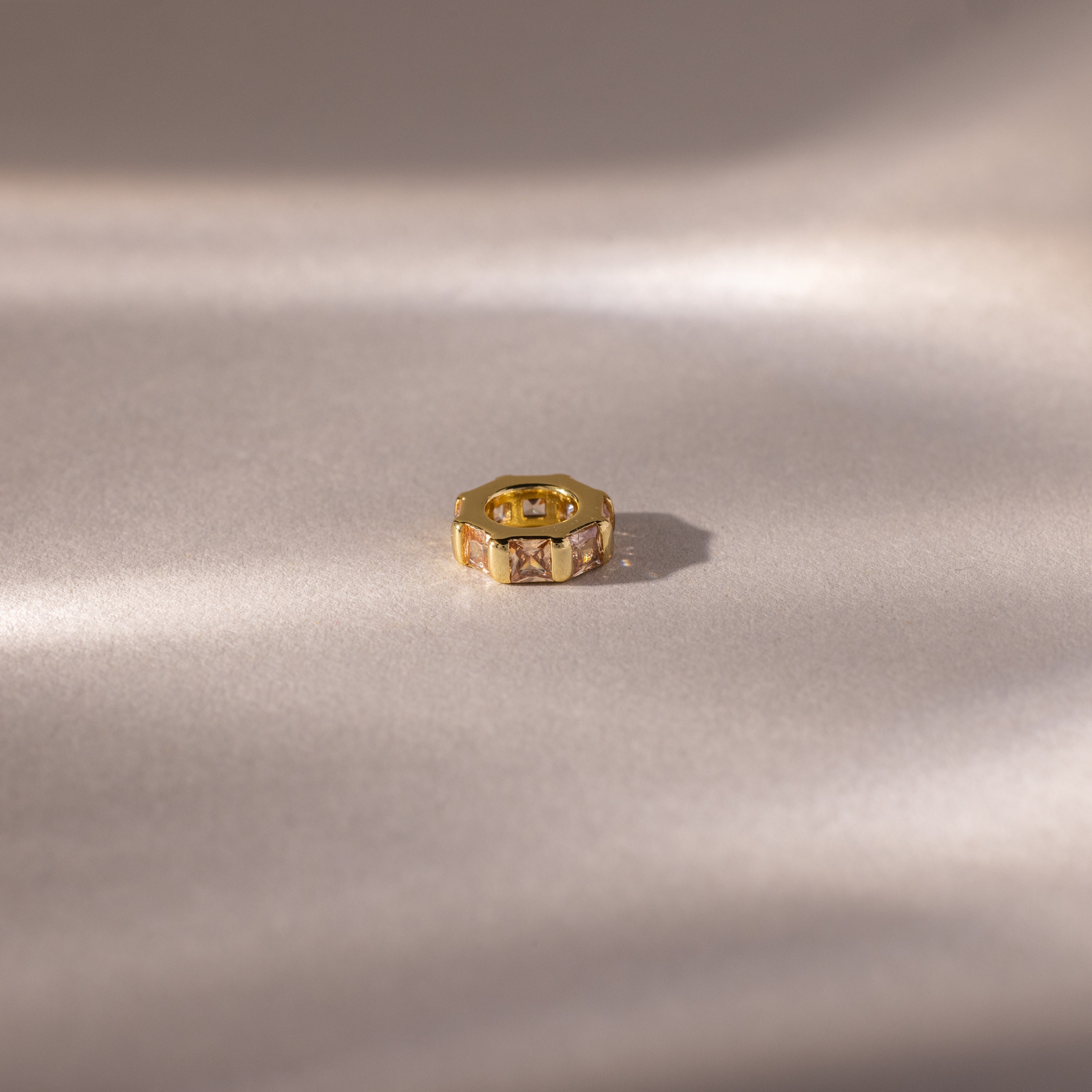 The Infinity Princess Topaz Charm rests on a soft, reflective surface, illuminated by gentle light and shadows.