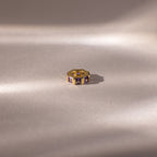 Gold ring with princess-cut, rich purple stones like the Infinity Princess Amethyst Charm, displayed on a soft, light backdrop with gentle shadows.
