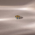 The Infinity Princess Blue Zircon Charm, featuring princess-cut blue stones, is elegantly displayed on a soft beige surface with gentle lighting—a stylish tribute to timeless design.