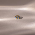 The Infinity Princess Blue Zircon Charm, featuring princess-cut blue stones, is elegantly displayed on a soft beige surface with gentle lighting—a stylish tribute to timeless design.