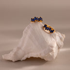 Staggered Baguette Sapphire Huggies displayed on a white seashell, featuring modern gold earrings with baguette-cut blue sapphires against a neutral background.