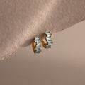 Staggered Baguette Aquamarine Huggies featuring rectangular aquamarine gemstones are shown on a soft, beige textured surface.