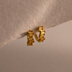 Staggered Baguette Topaz Huggies shine with modern elegance, featuring gold hoops accented by rectangular topaz gems, displayed on a textured off-white surface.