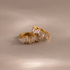 The Staggered Baguette Diamond Huggies, featuring gold hoops set with baguette-cut diamonds, rest on a soft beige surface—elegant modern earrings that add refined sparkle to any look.