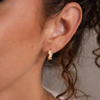 Close-up of a woman's ear wearing Staggered Baguette Birthstone Huggies—small gold hoops with rectangular baguette-cut stones for a modern, elegant look.