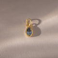 The Teardrop Aquamarine Charm features a blue teardrop birthstone in a gold bezel setting, showcased on a light beige background.