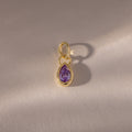 A close-up of the Teardrop Alexandrite Charm reveals its intricate gemstone set in a gold bezel setting.