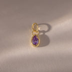 A close-up of the Teardrop Alexandrite Charm reveals its intricate gemstone set in a gold bezel setting.
