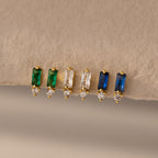Three pairs of Baguette Birthstone Drop Studs: gold earrings with green, clear, and blue baguette stones, each accented by a tiny diamond.