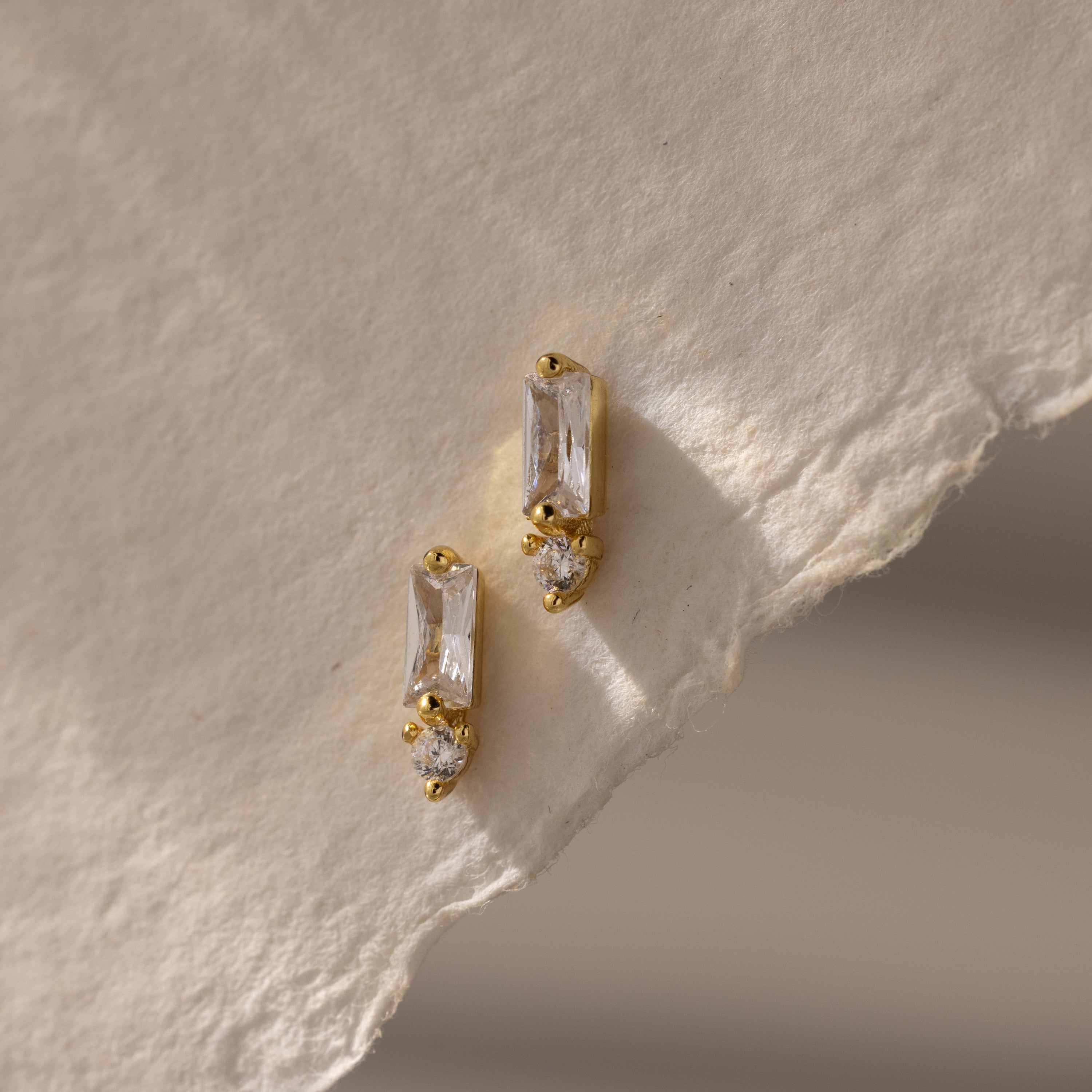 Baguette Diamond Drop Studs with rectangular and round clear stones displayed on textured off-white paper—ideal for those looking for modern, elegant jewelry.