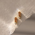 Baguette Topaz Drop Studs: gold earrings with rectangular peach topaz and small round diamonds, styled on textured paper. The perfect touch of elegant birthstone jewelry.