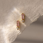 Baguette Pink Tourmaline Drop Studs: Modern gold earrings with pink rectangular tourmaline and small clear stones, displayed on textured paper, bringing a fresh update to classic birthstone earrings.