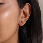 Close-up of a woman's ear with straight dark hair, wearing Baguette Blue Zircon Drop Studs—perfect modern elegant earrings for those who love blue and gold or birthstone jewelry.