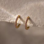 Pink Tourmaline Clicker Huggies—gold hoop earrings adorned with small pink tourmaline gemstones, ideal for daily wear, shown resting on a soft textured fabric.
