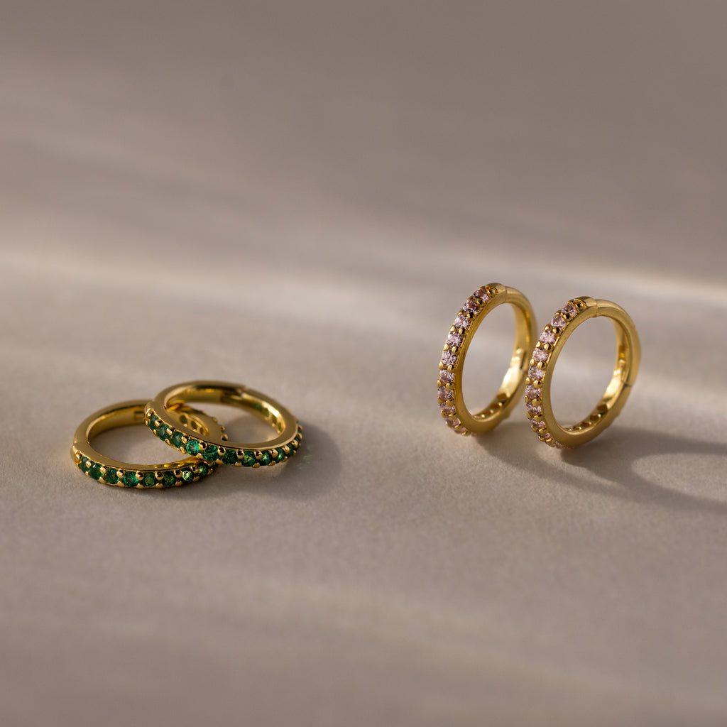 Two pairs of gold hoop earrings, including Pink Tourmaline Clicker Huggies, rest on a beige surface—ideal as birthstone earrings or for everyday huggie style.