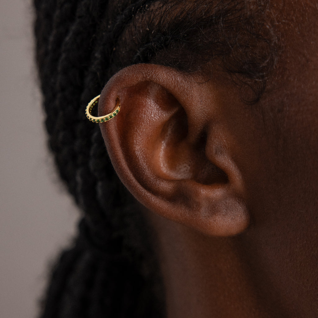 Close-up of an ear wearing Birthstone Clicker Huggies, elegant gold hoop earrings ideal for daily wear; braided hair appears in the background.