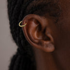 Close-up of an ear wearing Birthstone Clicker Huggies, elegant gold hoop earrings ideal for daily wear; braided hair appears in the background.
