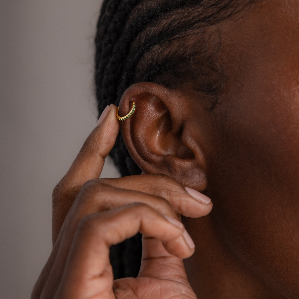 A person touches their ear, which features a Birthstone Clicker Huggie in the cartilage—an elegant and subtle piece of everyday jewelry.