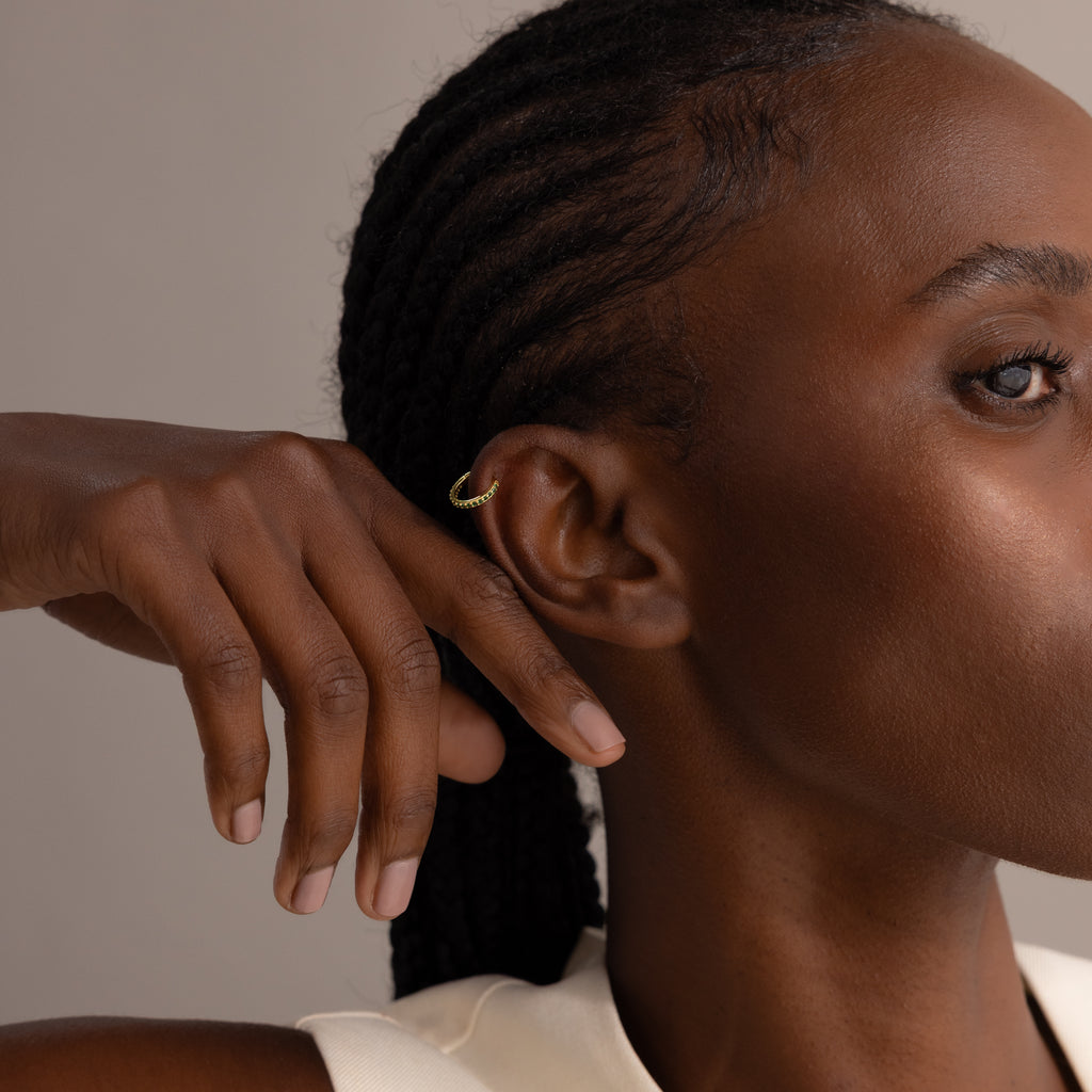 A woman with braided hair shows off Pink Tourmaline Clicker Huggies and a small gold ear cuff, her hand raised near her face.