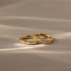 Two Diamond Clicker Huggies with small diamonds rest on a soft, beige surface in gentle light—perfect for pairing with your favorite everyday earrings.