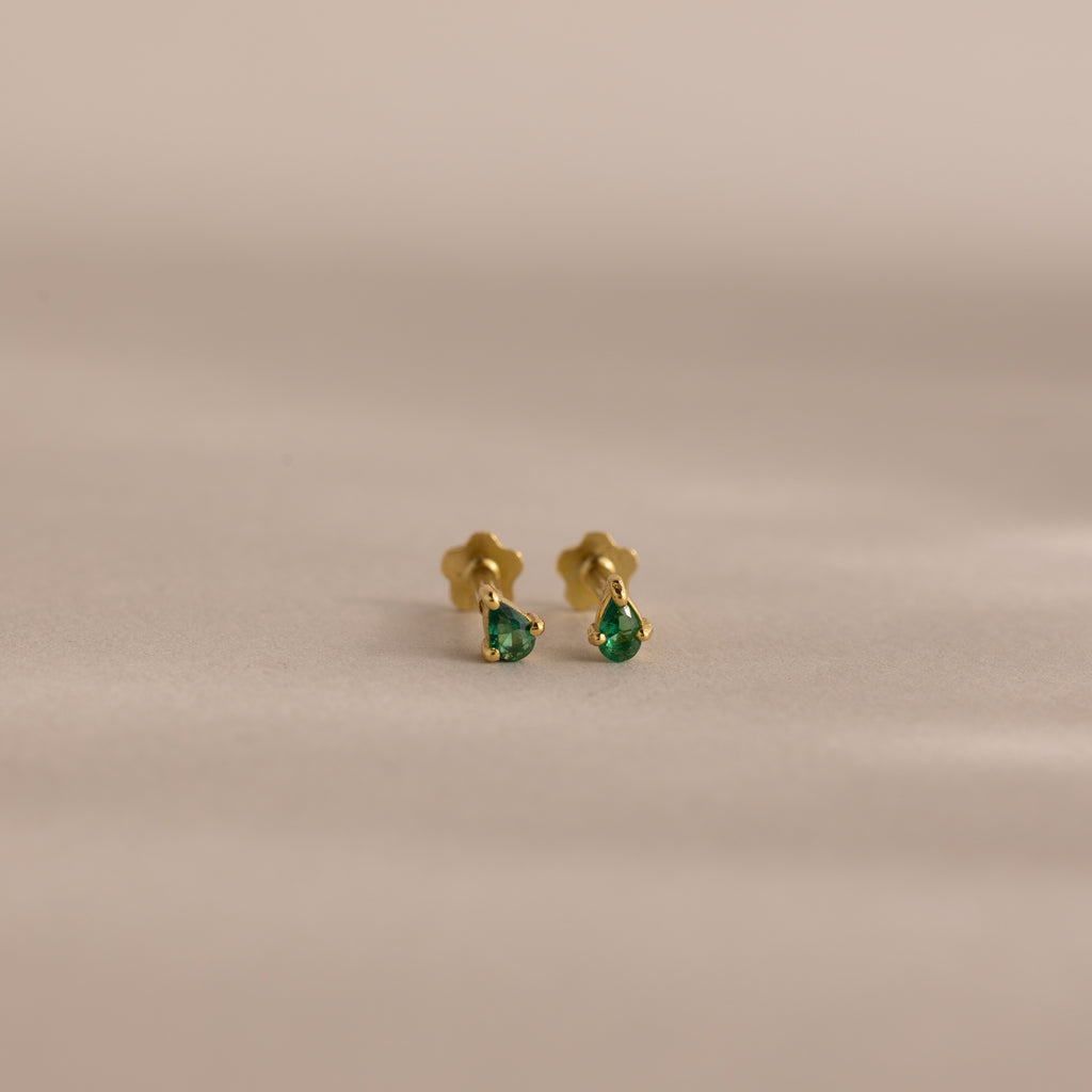 The Teardrop Emerald Flatback Studs are small gold earrings with green gemstone drops, offering elegant birthstone jewelry displayed on a plain, neutral background.