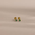 The Teardrop Emerald Flatback Studs are small gold earrings with green gemstone drops, offering elegant birthstone jewelry displayed on a plain, neutral background.