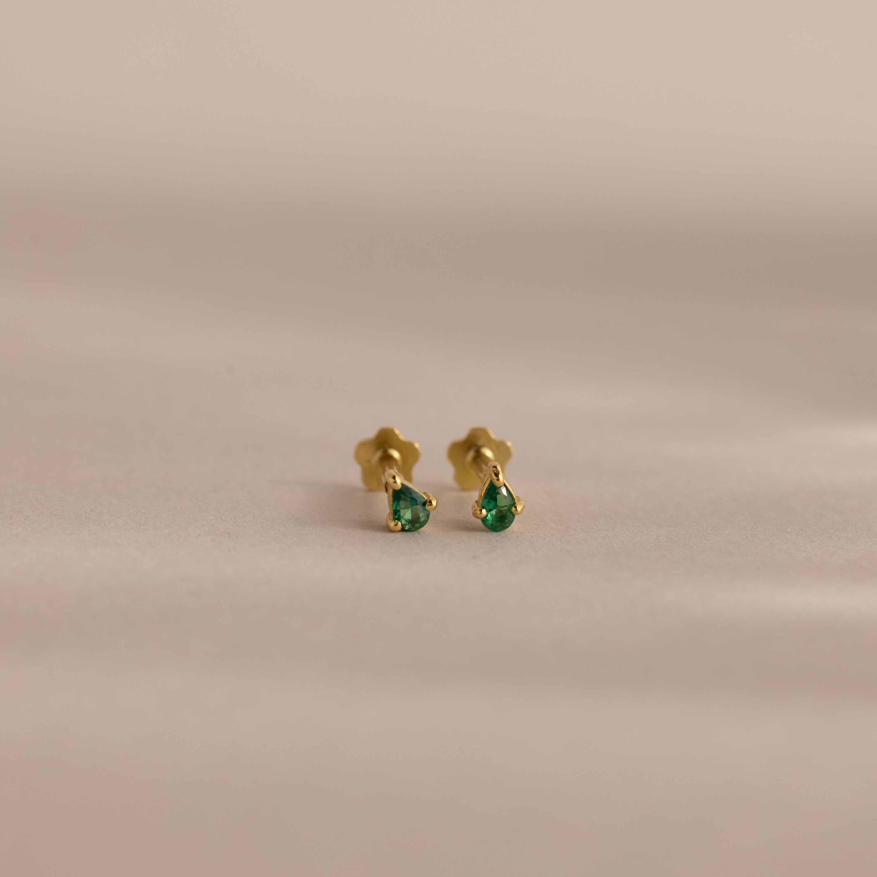 The Teardrop Emerald Flatback Studs are small gold earrings with green gemstone drops, offering elegant birthstone jewelry displayed on a plain, neutral background.