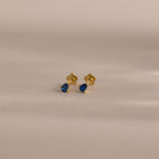 Teardrop Sapphire Flatback Studs featuring gold and small blue teardrop gems—a stunning piece of birthstone jewelry, showcased on a neutral background.