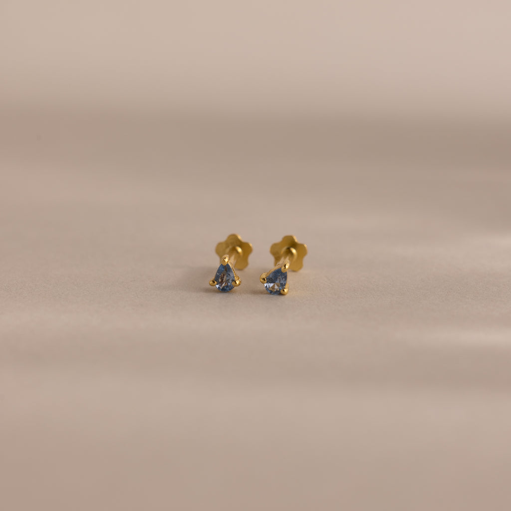Teardrop Aquamarine Flatback Studs—small gold earrings with vibrant blue gemstone centers, shown on a softly lit neutral background—a timeless birthstone jewelry piece.