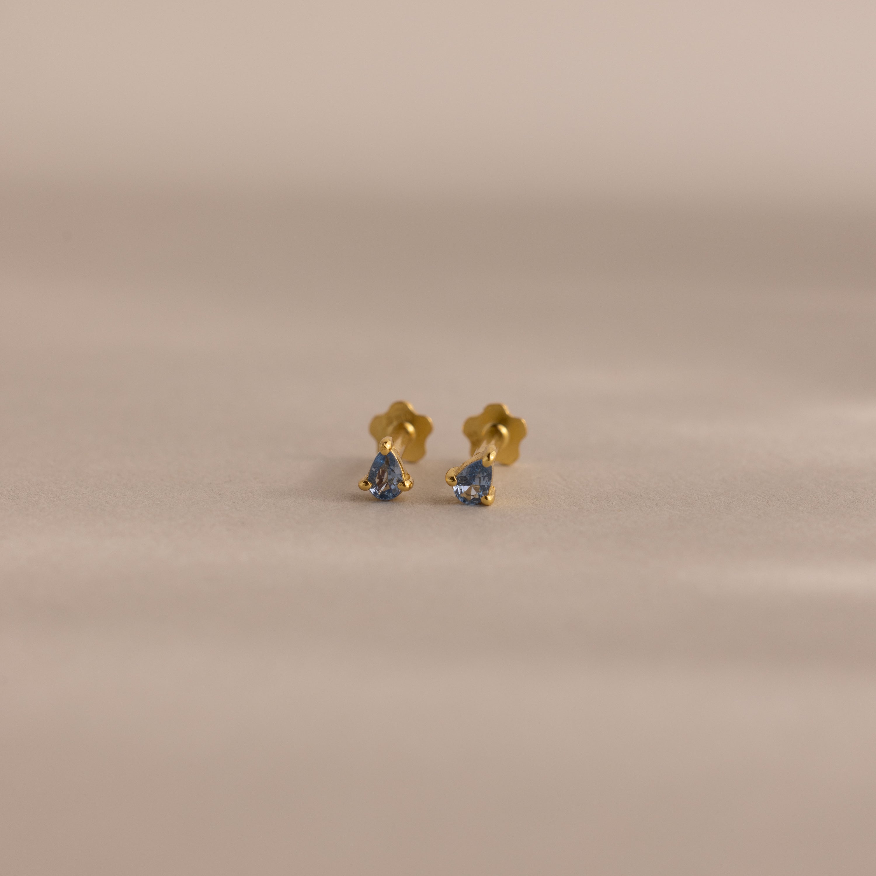 Teardrop Aquamarine Flatback Studs—small gold earrings with vibrant blue gemstone centers, shown on a softly lit neutral background—a timeless birthstone jewelry piece.