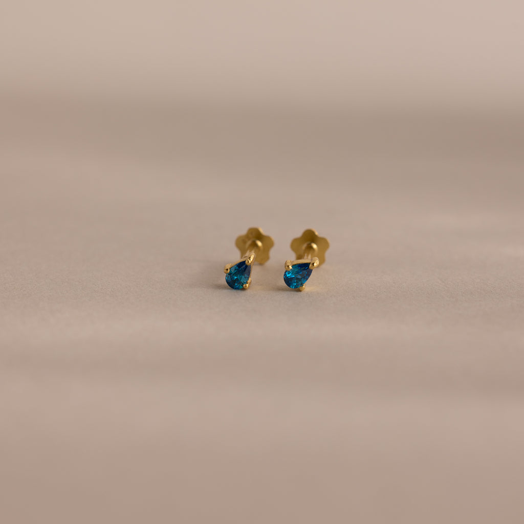 Teardrop Blue Zircon Flatback Studs: gold earrings featuring teardrop-shaped blue zircon gemstones, perfect for elegant birthstone jewelry lovers. Displayed on a neutral background.
