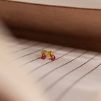Teardrop Ruby Flatback Studs, charming gold earrings with small pink teardrop stones, displayed on a striped white surface.