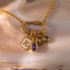 Gold chain necklace with charms—a letter K, Teardrop Blue Zircon Charm, star symbol, and small round charm—displayed on a shell background. A unique gemstone jewelry piece perfect for showcasing your personal style.