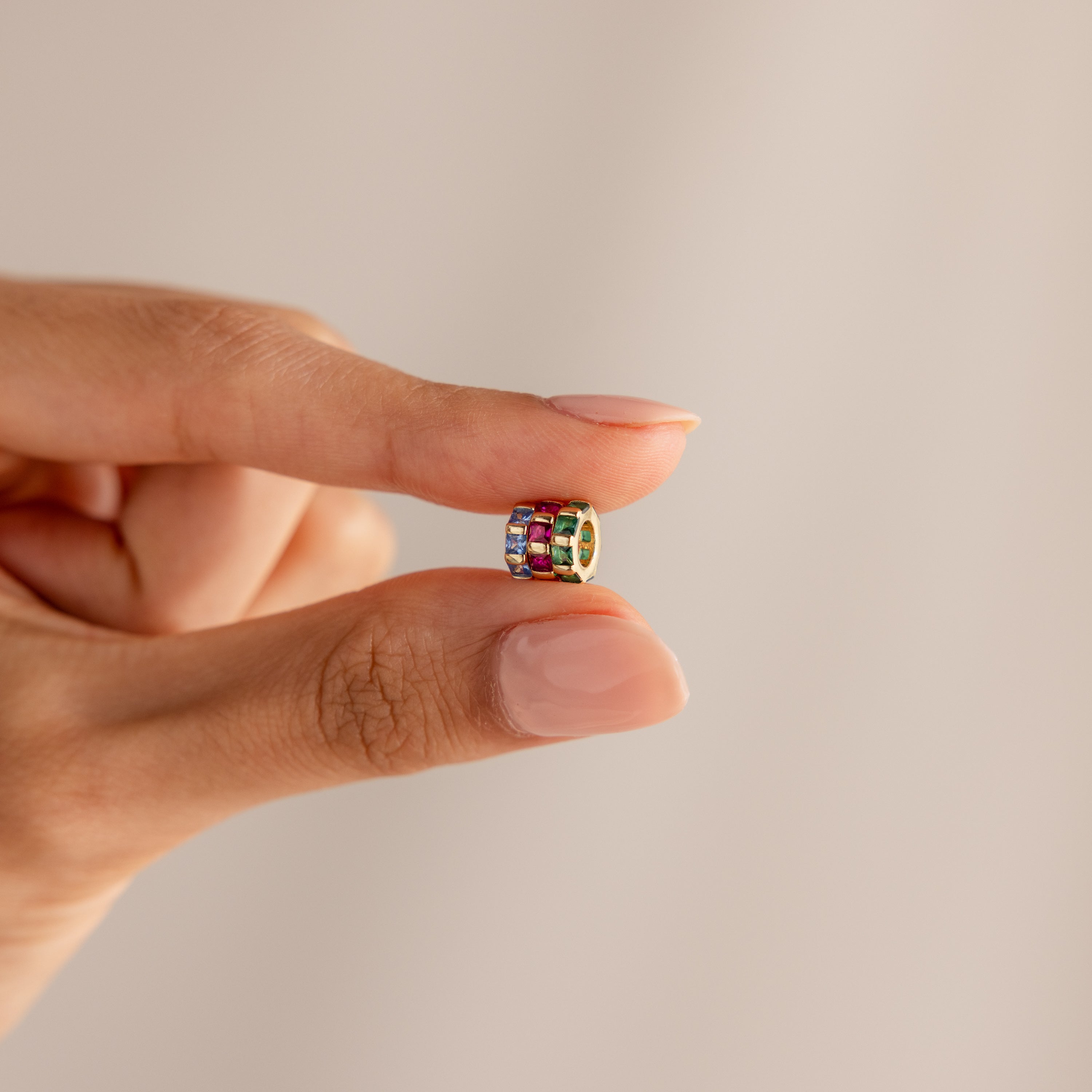 A hand holds the Infinity Princess Birthstone Charm ring, featuring vibrant princess-cut stones, delicately balanced between the thumb and index finger.
