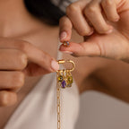 A woman’s hands attach the Infinity Princess Birthstone Charm to a gold chain bracelet, which sparkles with colorful, princess-cut stones.