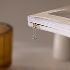 The Duo Birthstone Drop Studs rest on the edge of a closed book, their delicate design and sparkling stones catching the light beautifully.