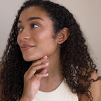 A woman with curly hair, smiling and looking to the side, wears a sleeveless top and the Duo Birthstone Drop Studs.