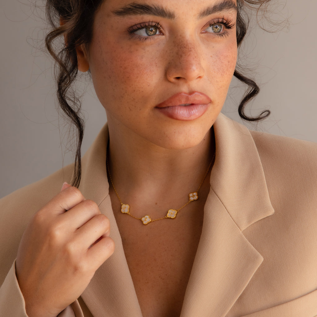 A person wearing a beige blazer and the Gemstone Clover Letter Necklace with four floral pendants, looking slightly to the side.