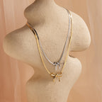 The Herringbone Bow Necklace in Sterling Silver is elegantly displayed on a beige mannequin against a soft, neutral background, highlighting its sleek, coquette-inspired style.