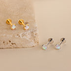 Two pairs of Opal Flat Back Studs—one gold, one silver—rest on a beige stone surface. These dainty earrings are perfect for everyday wear as elegant sleeper back studs.