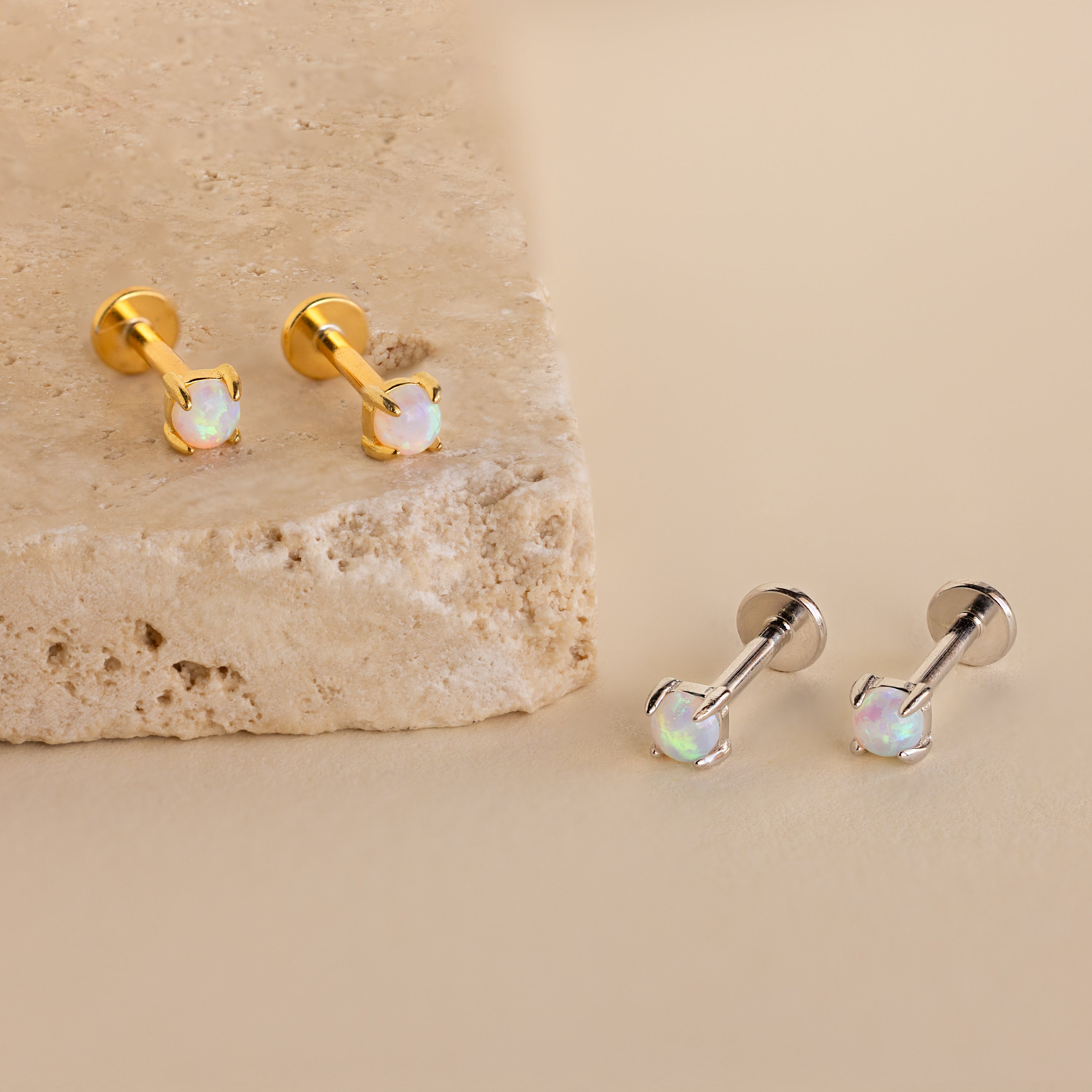 Two pairs of Opal Flat Back Studs—one gold, one silver—rest on a beige stone surface. These dainty earrings are perfect for everyday wear as elegant sleeper back studs.
