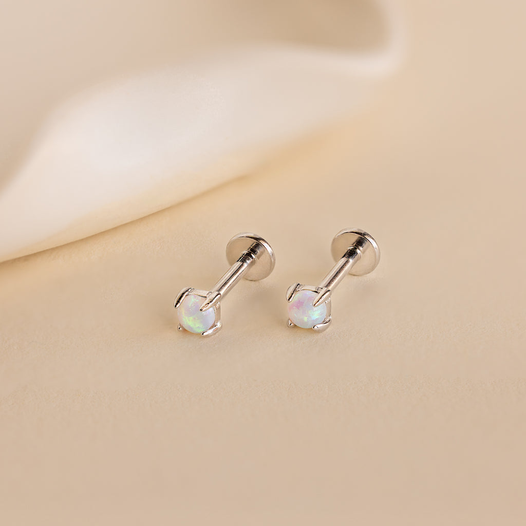 The Opal Flat Back Studs in Sterling Silver are comfortable sleeper earrings featuring round opal gemstones, displayed as silver studs on a light beige surface.