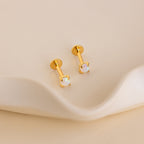 Opal Flat Back Studs with round opal stones displayed on a wavy, cream-colored surface—dainty earrings ideal for effortless elegance.