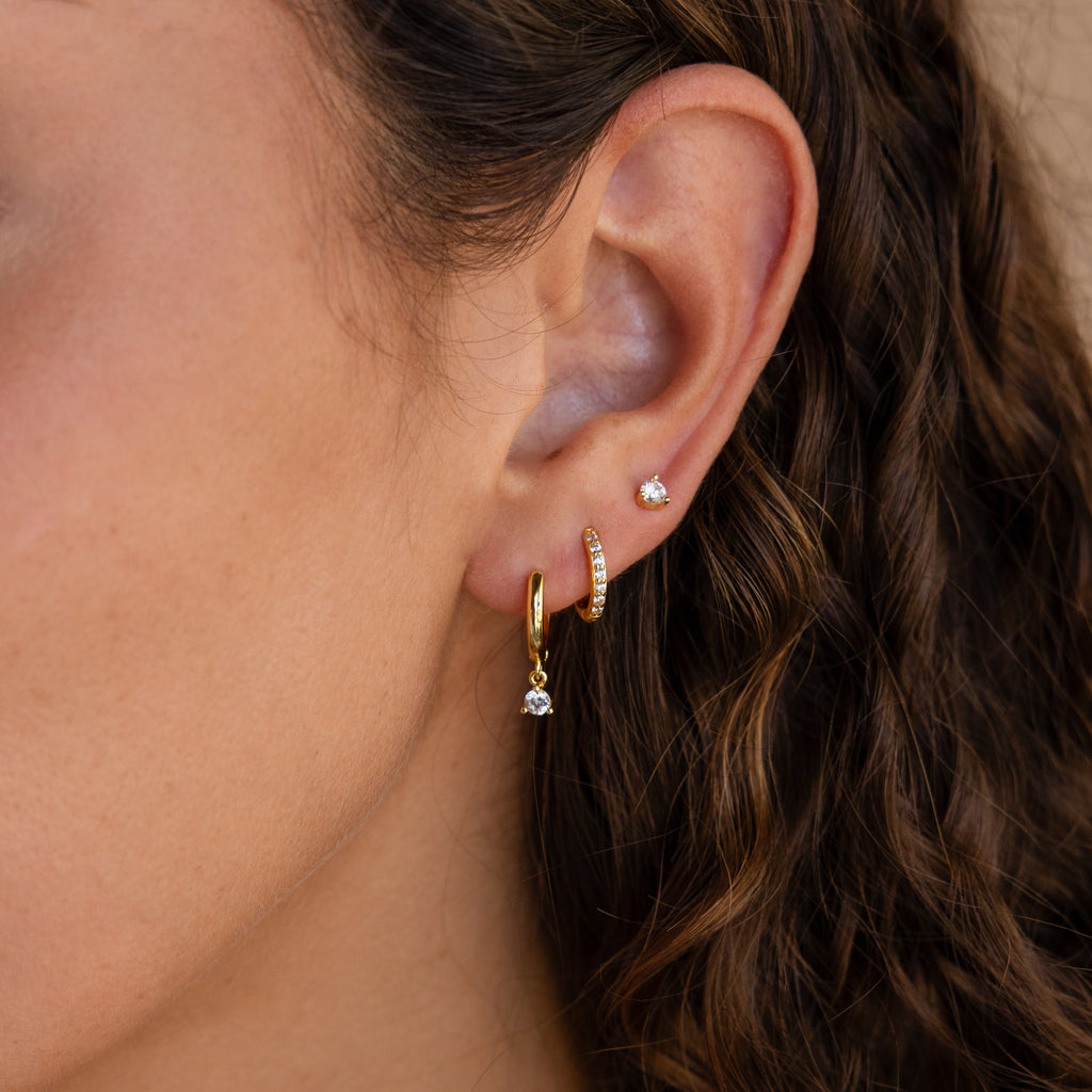 Close-up of a woman's ear wearing three gold earrings and one stud against curly brown hair—perfect for highlighting the Classic Diamond Earrings Set in 18K Gold on a special occasion.