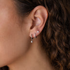 Close-up of an ear with three silver hoops and a classic stud from the Classic Diamond Earrings Set, next to curly brown hair.
